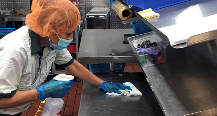 A Delta catering employee in PPE washes down a food preparation counter